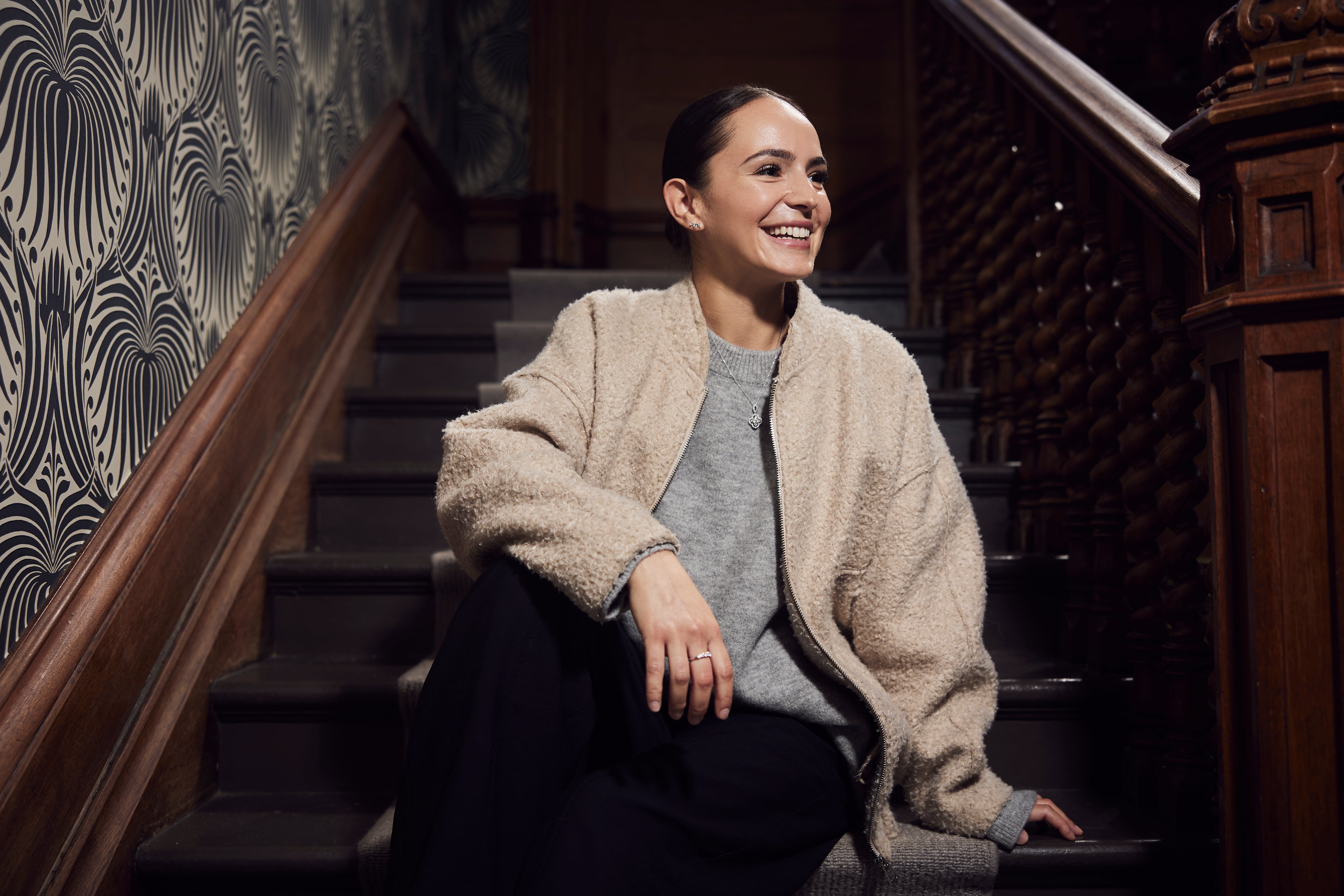 Woman wearing a diamond pendant necklace, earrings and ring in a lifestyle portrait at Robins + Robins jewellers in Plymouth.