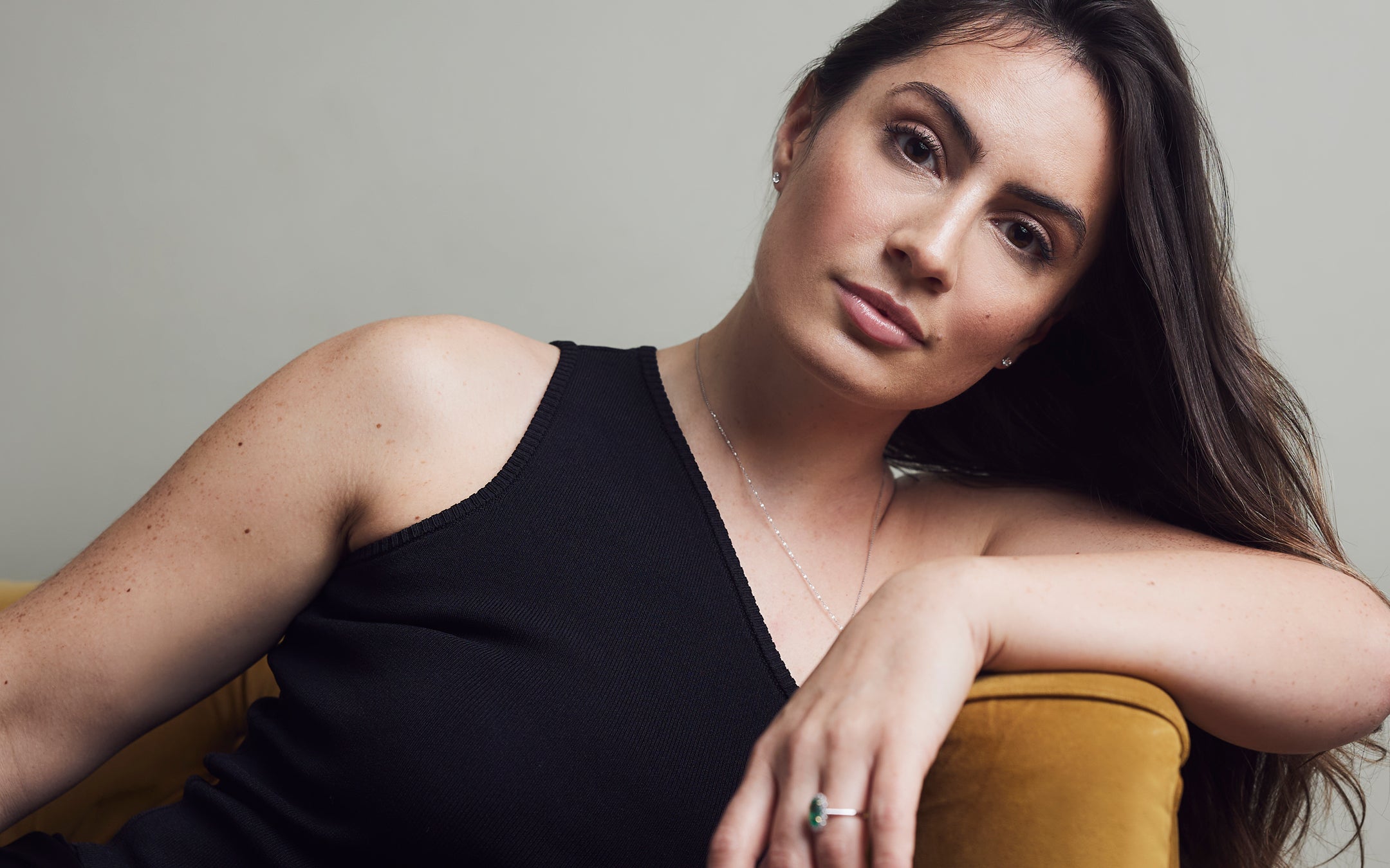 Woman reclining on a sofa wearing an emerald ring and delicate necklace