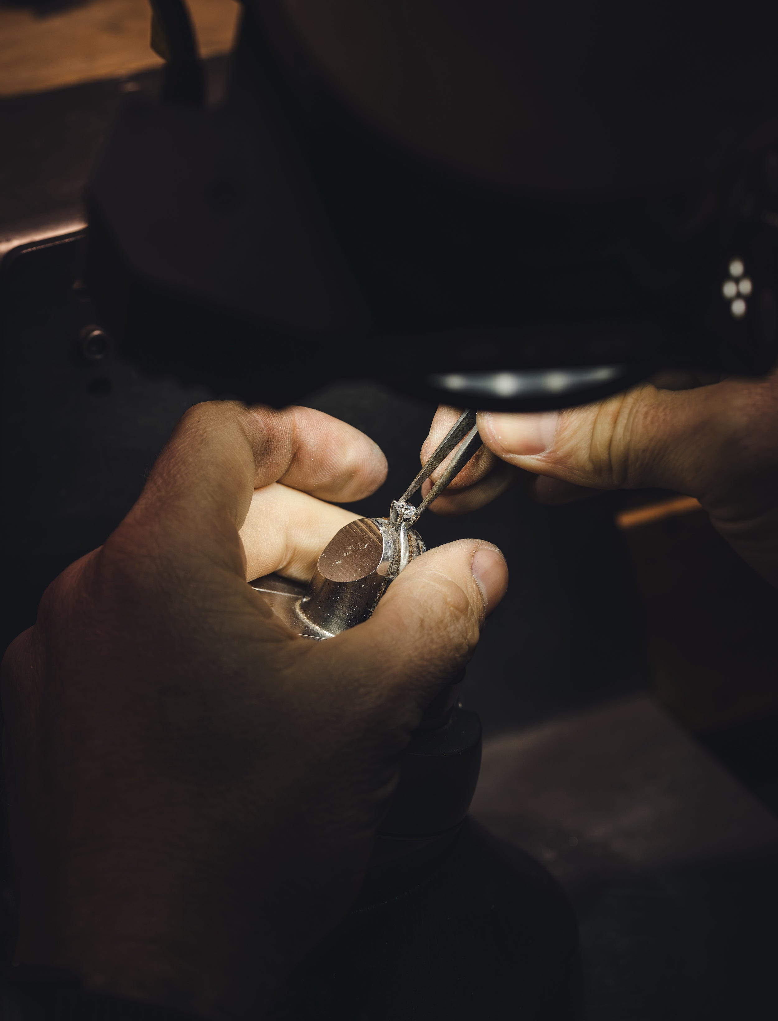 Close-up of hands working on a diamond engagement ring with a dark background