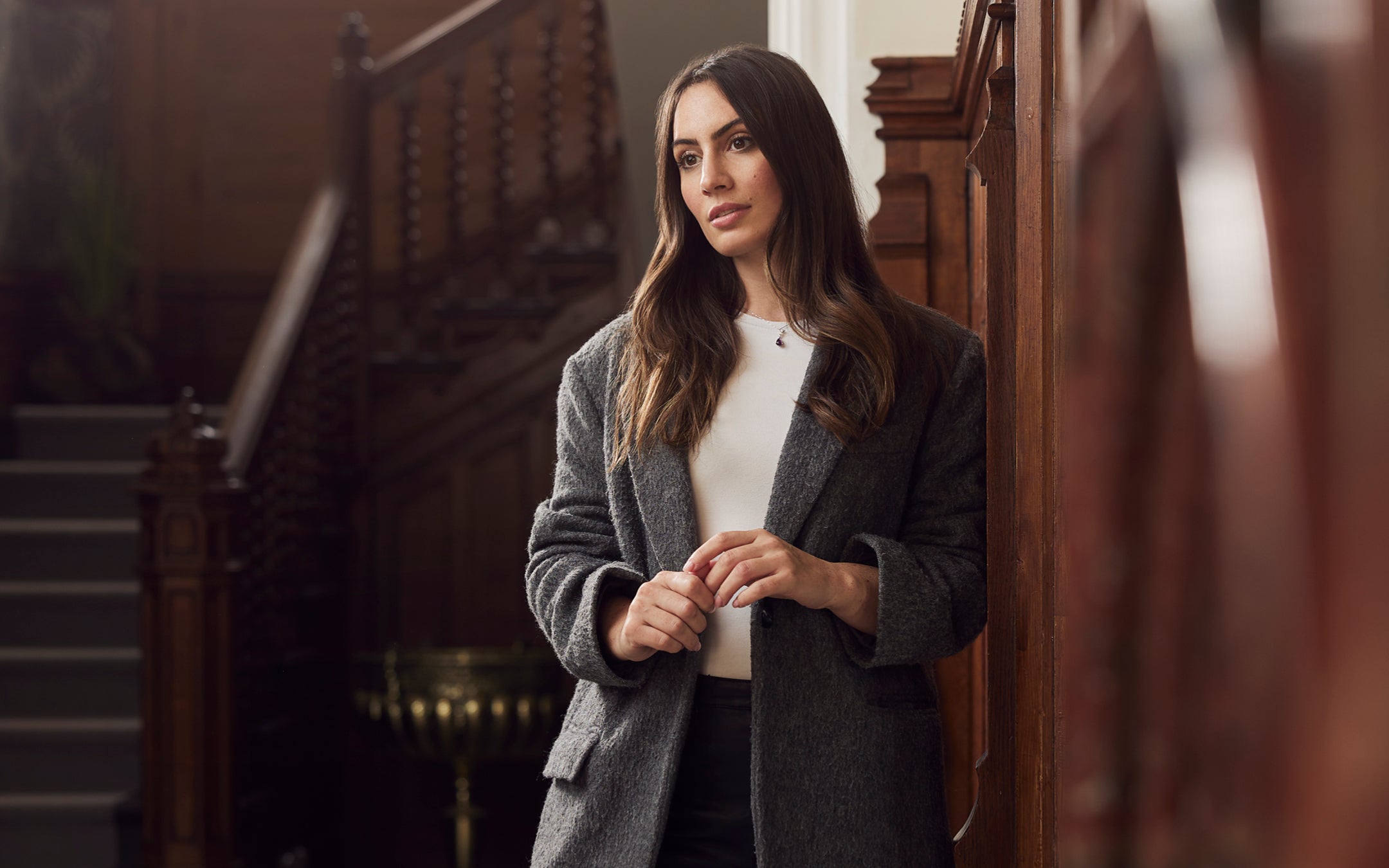 Woman wearing jewellery in Plymouth. Wearing a delicate pendant necklace with a grey coat, looking thoughtfully ahead.